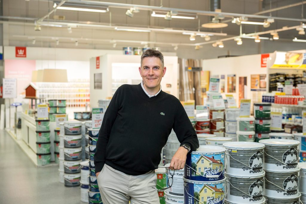Henkilö seisoo myymälätilassa maalipurkkien ja hyllyjen keskellä, taustalla valaistu liike-ympäristö.