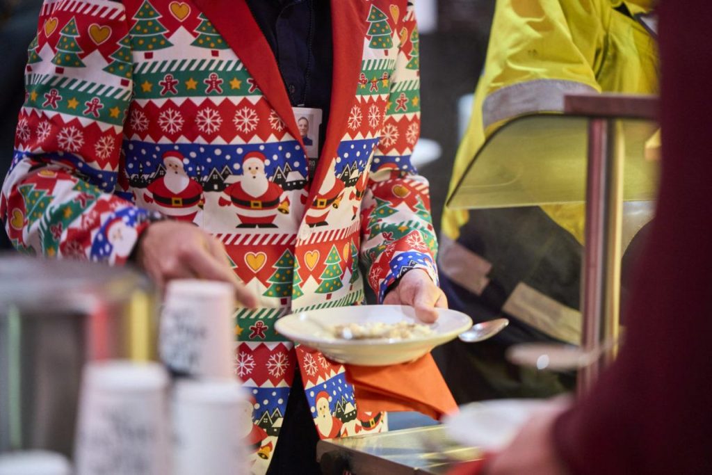 Tarjoilutilanne tapahtumassa, henkilö ojentaa lautasta ruokalinjaston äärellä, yllään värikäs kuviollinen asu.