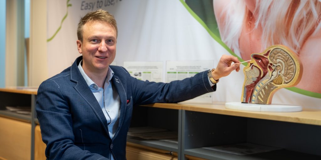Henkilö esittelee pään anatomiamallia sisätilassa hyllyn äärellä, taustalla esittelymateriaalia.