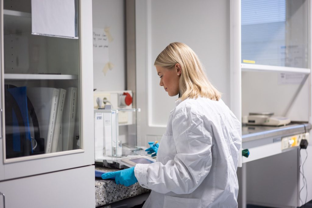 Henkilö työskentelee laboratoriossa vaa’an ja mittauslaitteiden äärellä, ympärillä kaappeja ja työpintoja.