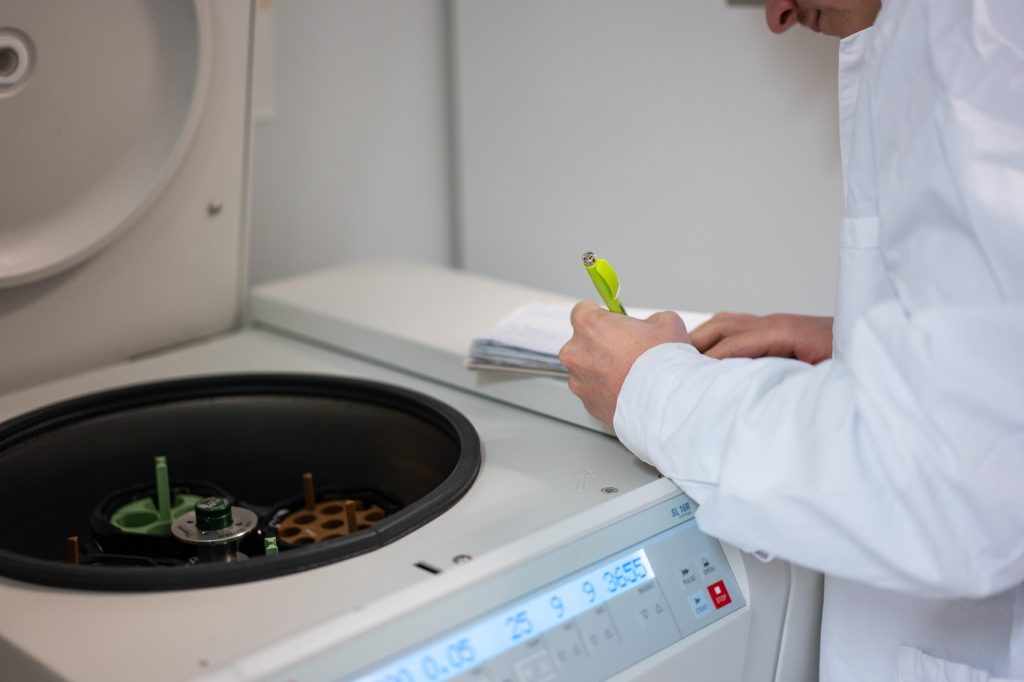 Lähikuva laboratoriotyöpisteestä, sentrifugi avoinna ja henkilö pitää kädessään muistivälinettä laitteen vieressä.