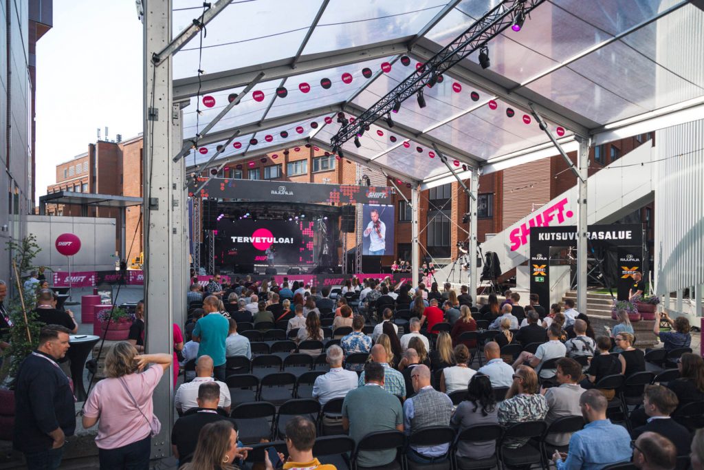 Yleisö istuu tuoleilla ja seuraa esitystä SHIFT businessfestivaalin päälavalla katetussa ulkotilassa.