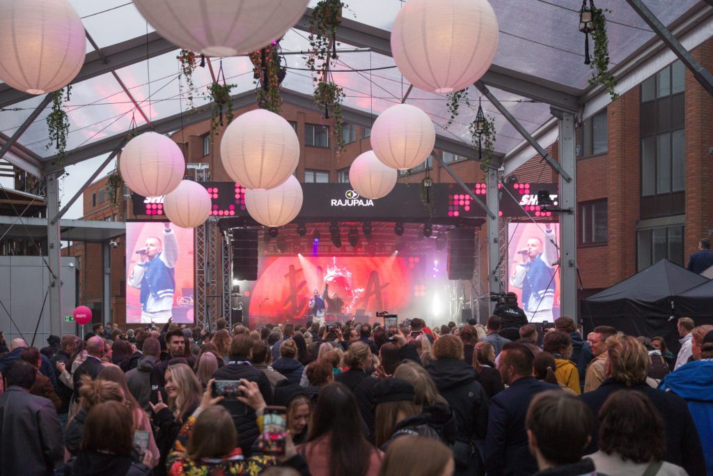 Täysi yleisö seuraa live‑esitystä SHIFT businessfestivaalin lavalla, yläpuolella riippuvat valaisimet ja esiintymistekniikka.